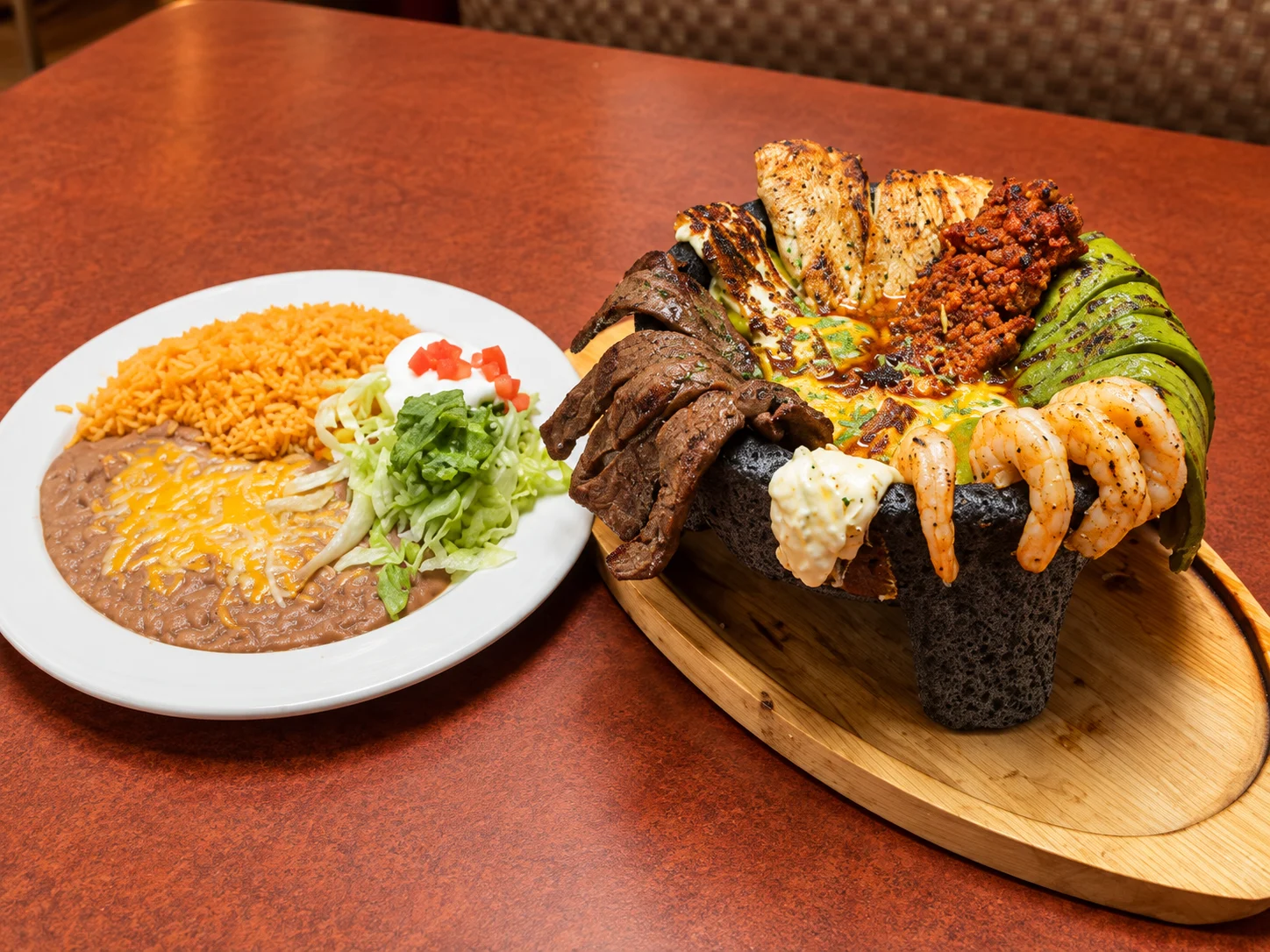 Traditional molcajete filled with grilled meats, shrimp, cactus, and melted cheese beside rice and beans